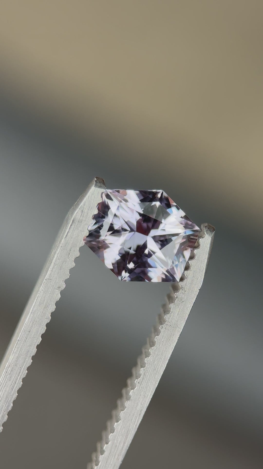Hexagonal sapphire placed on tweezers blurred background with visible purple-grey color change