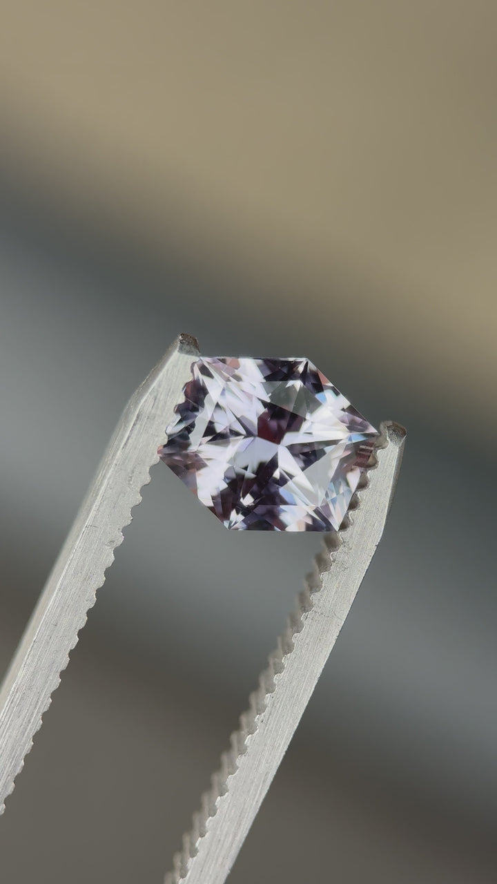 Hexagonal sapphire placed on tweezers blurred background with visible purple-grey color change