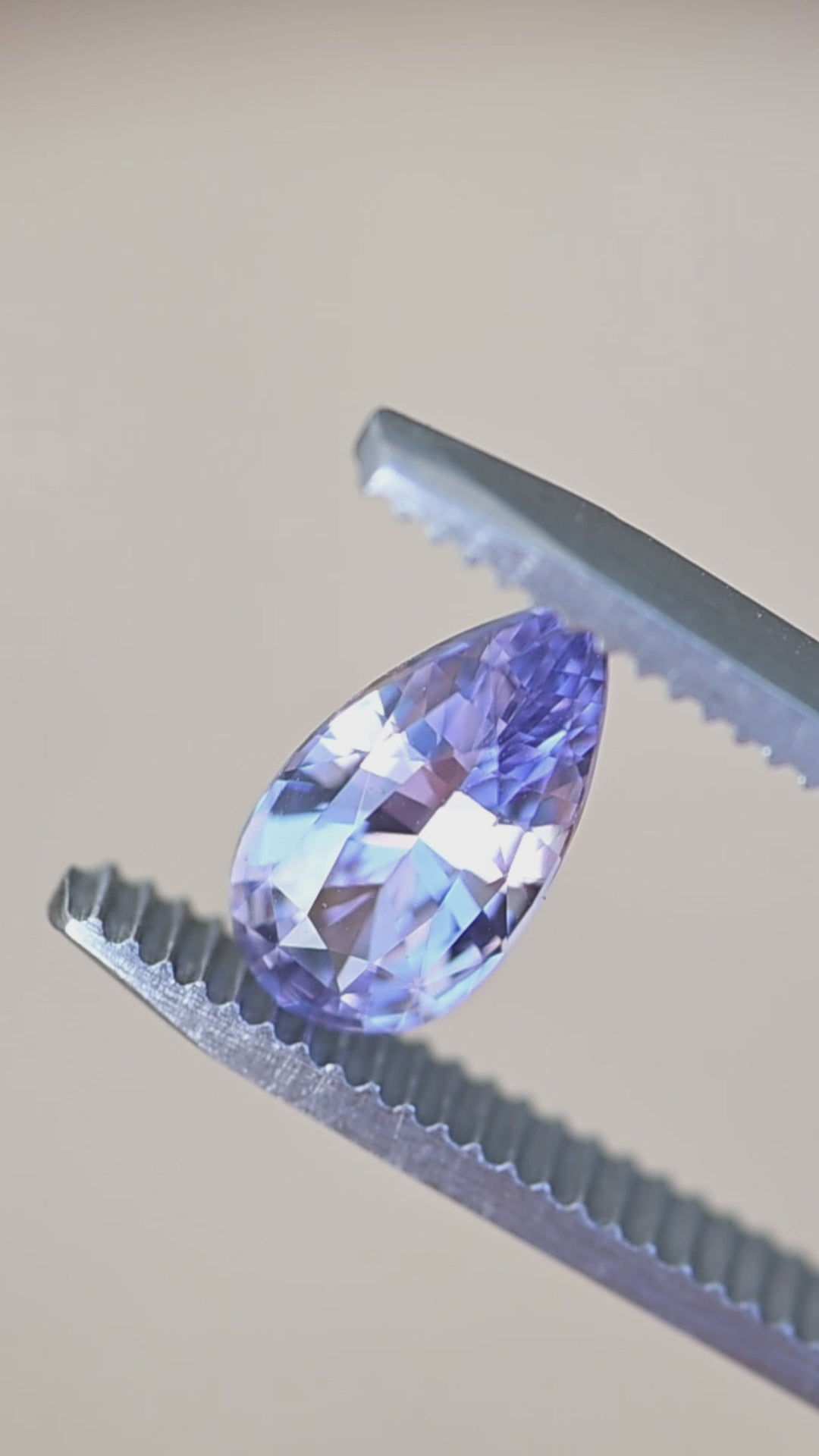 Rotating lavender pinkish purple sapphire in tweezers showing brilliance, color shifts, and precision pear cut from Madagascar.