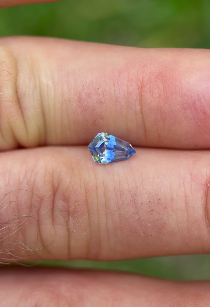 1.04-carat heated Parti sapphire shown on hand in sunlight, capturing the contrast between its blue and near-colorless zones.