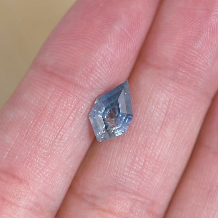 2.07ct Montana tablet shield sapphire rotating in hand, showing shifting blue saturation across the length of the stone and pronounced geometric facet reflections; parti zoning becomes more visible as light passes through the translucent areas.