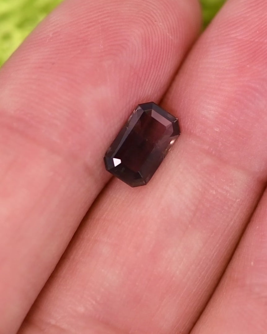 Close-up motion video of 1.34 carat purple, violet, and brown sapphire rotating under natural light, revealing brilliance, depth, and structure of its custom modified emerald cut, untreated gemstone from Umba River Valley, Tanzania.
