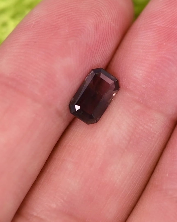 Close-up motion video of 1.34 carat purple, violet, and brown sapphire rotating under natural light, revealing brilliance, depth, and structure of its custom modified emerald cut, untreated gemstone from Umba River Valley, Tanzania.