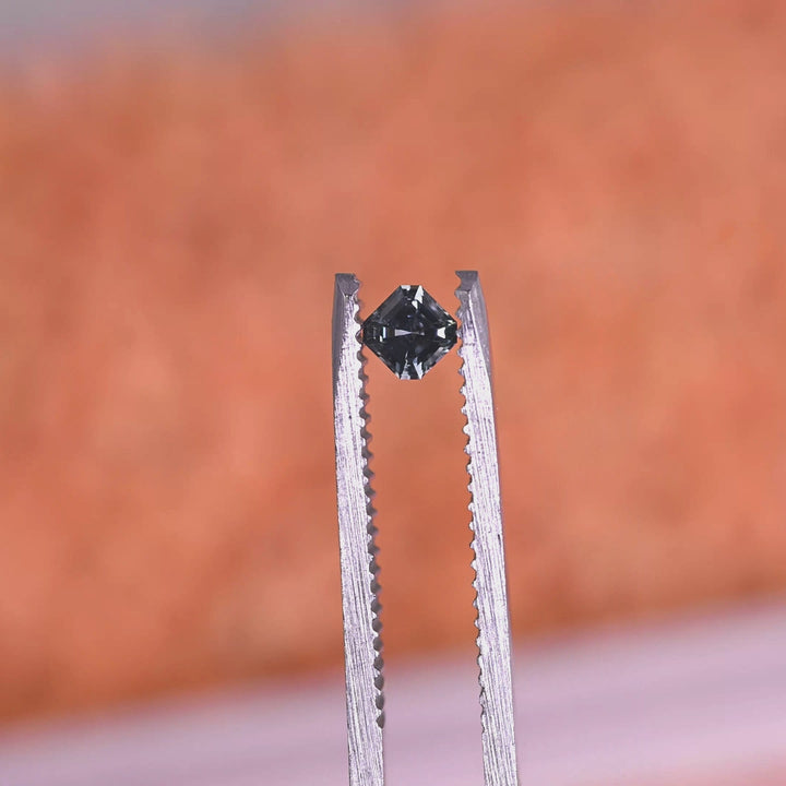 Loose Asscher cut Montana sapphire turning in tweezers, revealing the clean square geometry and blue to teal color shift in changing light.