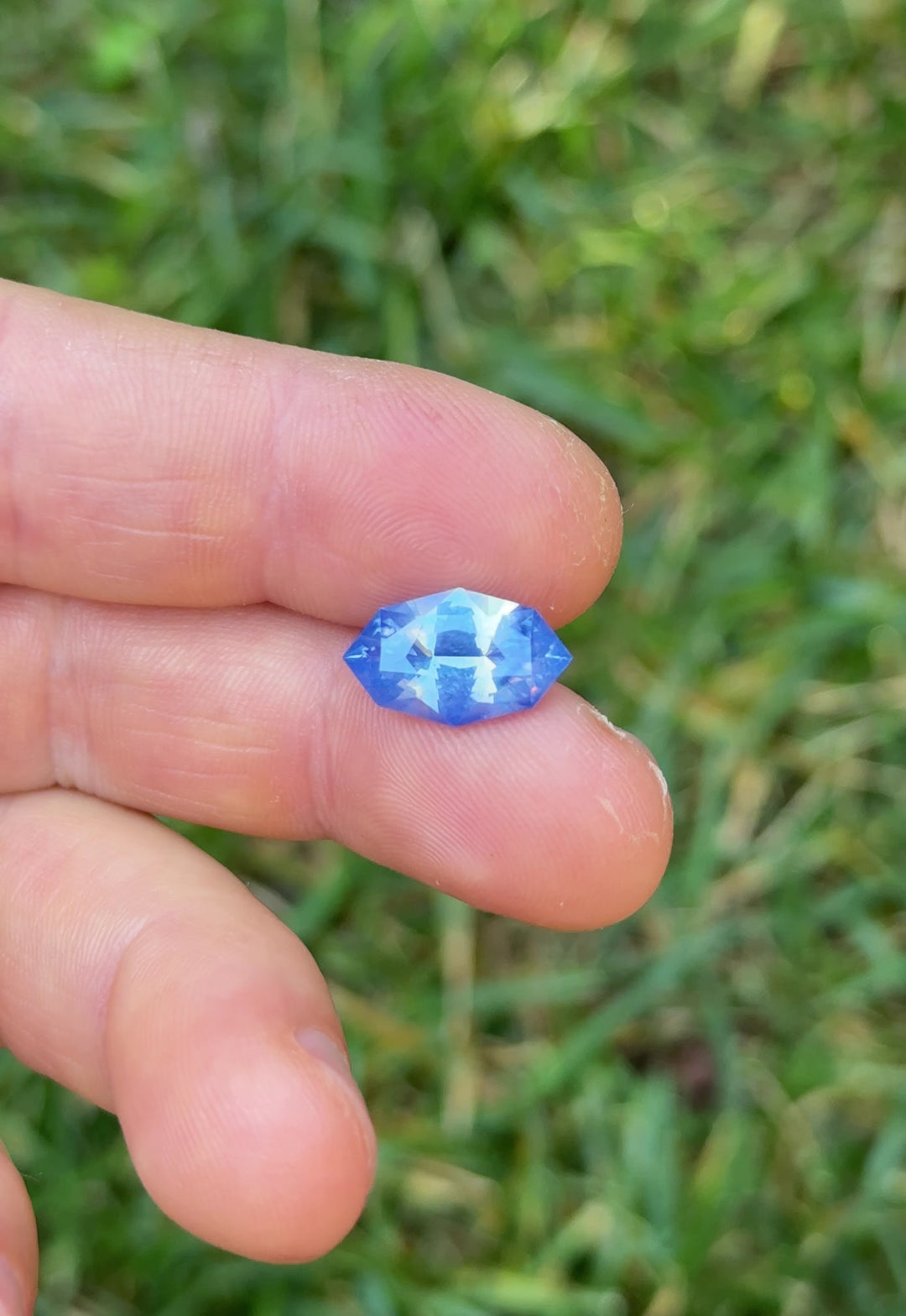 Macro video of 6.07 carat periwinkle blue sapphire resting on fingers, highlighting brilliance, opalescent glow, and reflective symmetry of the precision marquise mixed cut, untreated gemstone from Madagascar.