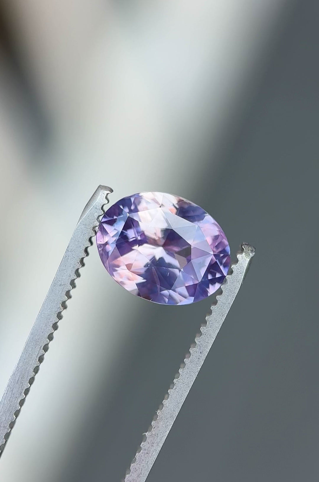Macro video of natural 4.04 carat oval cut sapphire highlighting brilliance, sparkle, and color variation between soft pink and violet hues under mixed lighting.