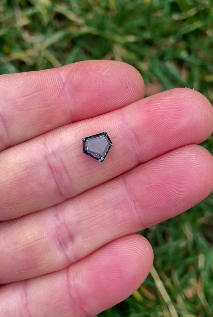 A 360-degree video showcasing a custom step cut shield sapphire weighing 1.70 carats, with stunning parti-colors of blue, green, and yellow, as it rotates in natural light to reveal its facets and clarity.
