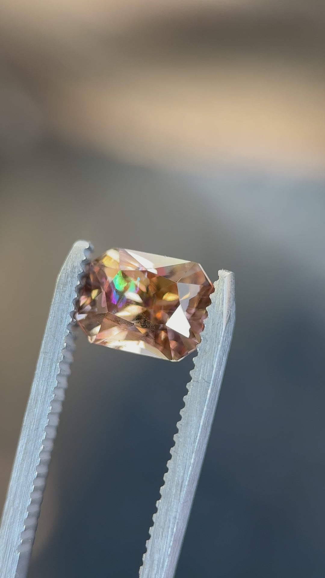 Close-up of a radiant cut Tanzanite showing brilliant reflections in purple, peach, and gold tones as it moves under direct light.