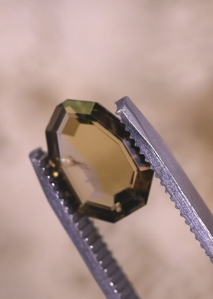 Video of a 3.20 carat untreated Tanzanite rotating in tweezers, revealing the custom shield portrait cut, step-cut facet reflections, and shifting pink, purple, and peach hues under natural light