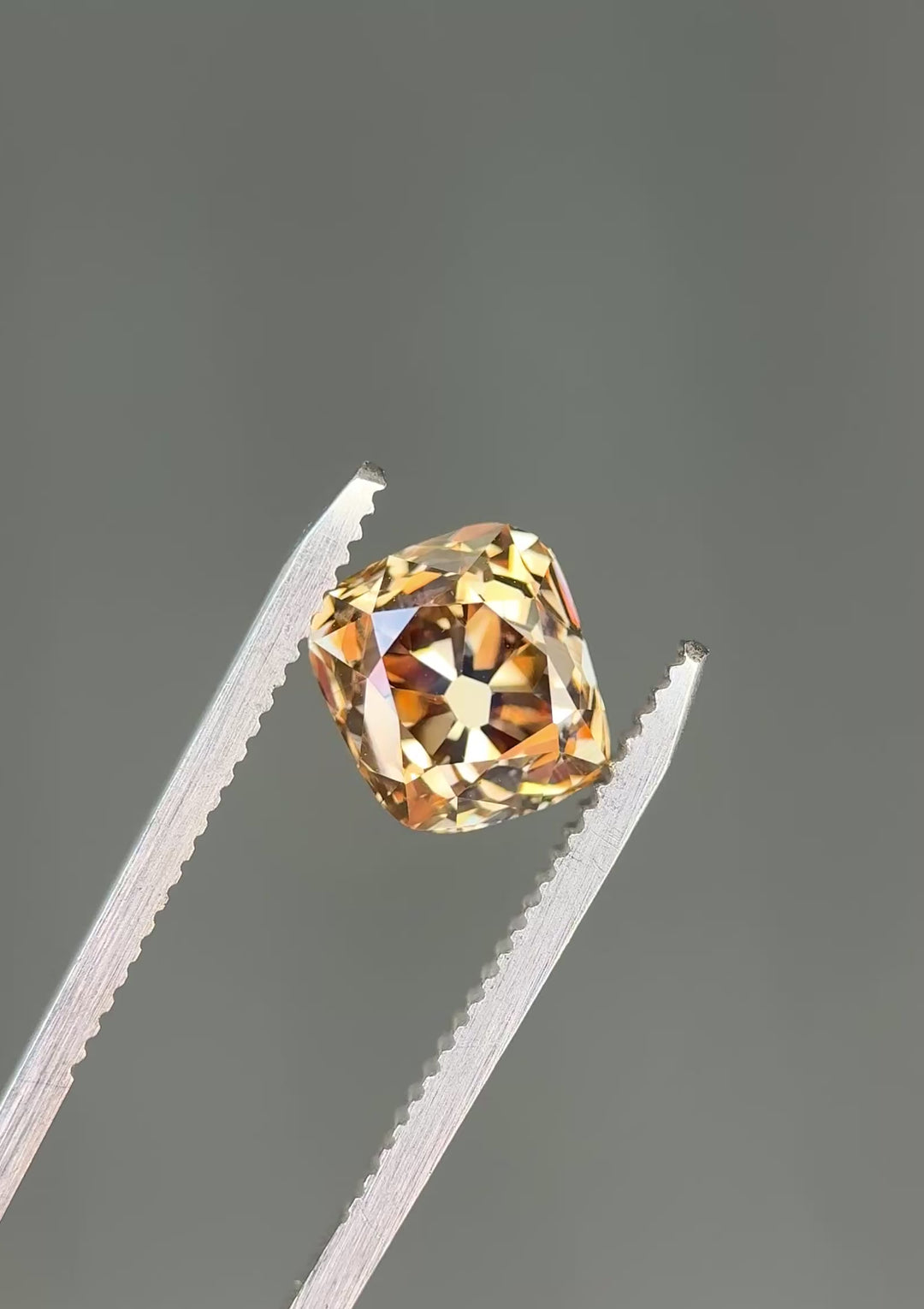 Macro video of a VVS1 Canadian champagne diamond turning in tweezers, showcasing broad vintage facets, exceptional clarity, and changing brown-gold reflections from every angle.