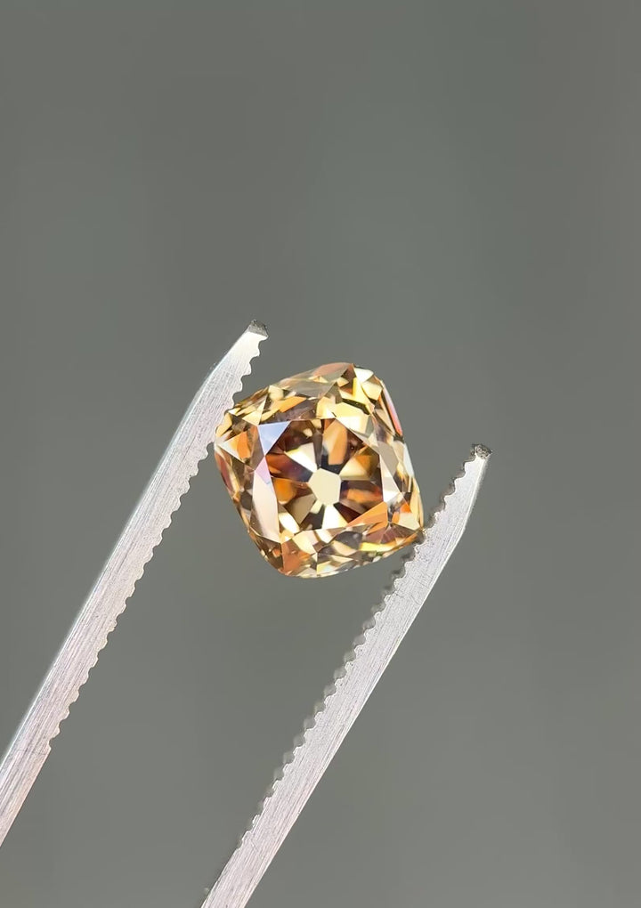 Macro video of a VVS1 Canadian champagne diamond turning in tweezers, showcasing broad vintage facets, exceptional clarity, and changing brown-gold reflections from every angle.