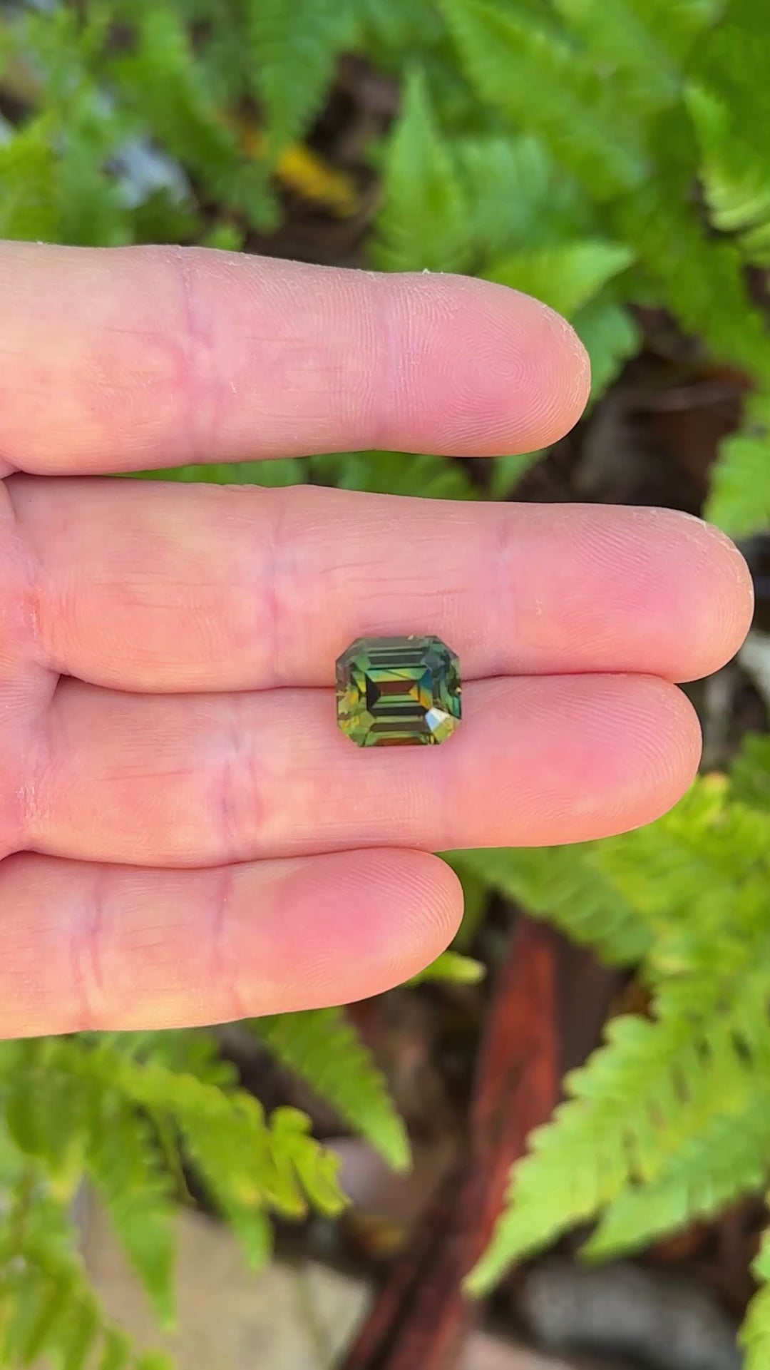 Detailed video of a 9.14 carat Nigerian parti sapphire emerald cut, captured under shifting light to reveal dynamic orange, yellow, blue, and green color zoning and crisp facet structure from Gombe, Nigeria