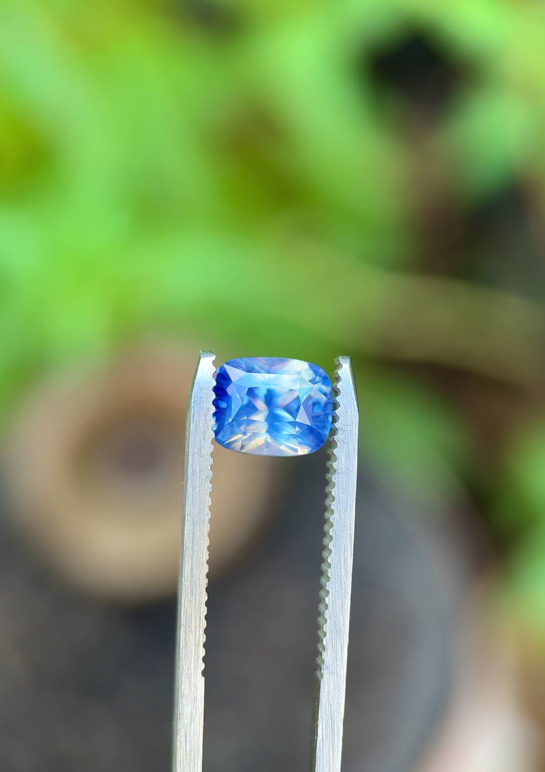 Video of 2.64CT parti blue and white sapphire rotating in gemstone tweezers, showing light play, internal glow, and opalescent color zoning of the mix cushion cut, unheated sapphire from Sakaraha, Madagascar.
