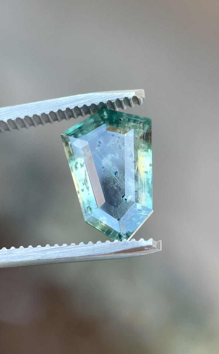 Video of a rotating 5.48-carat sapphire with a portrait shield cut, showing shifting yellow, teal, and blue tones under light.