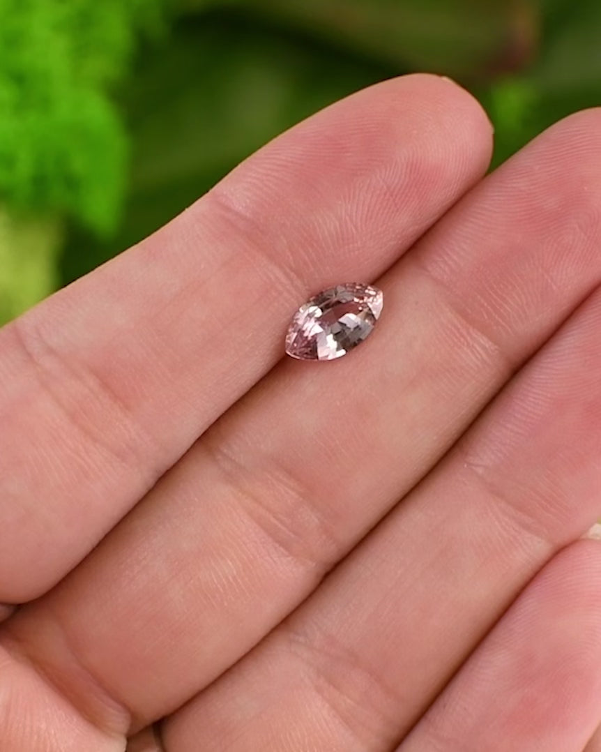 Close-up video of 1.32 carat peach and salmon pink sapphire on fingertip, showing shifting tones and reflections in daylight, showcasing the brilliance of the precision marquise mixed cut, untreated sapphire from Sakaraha, Madagascar.