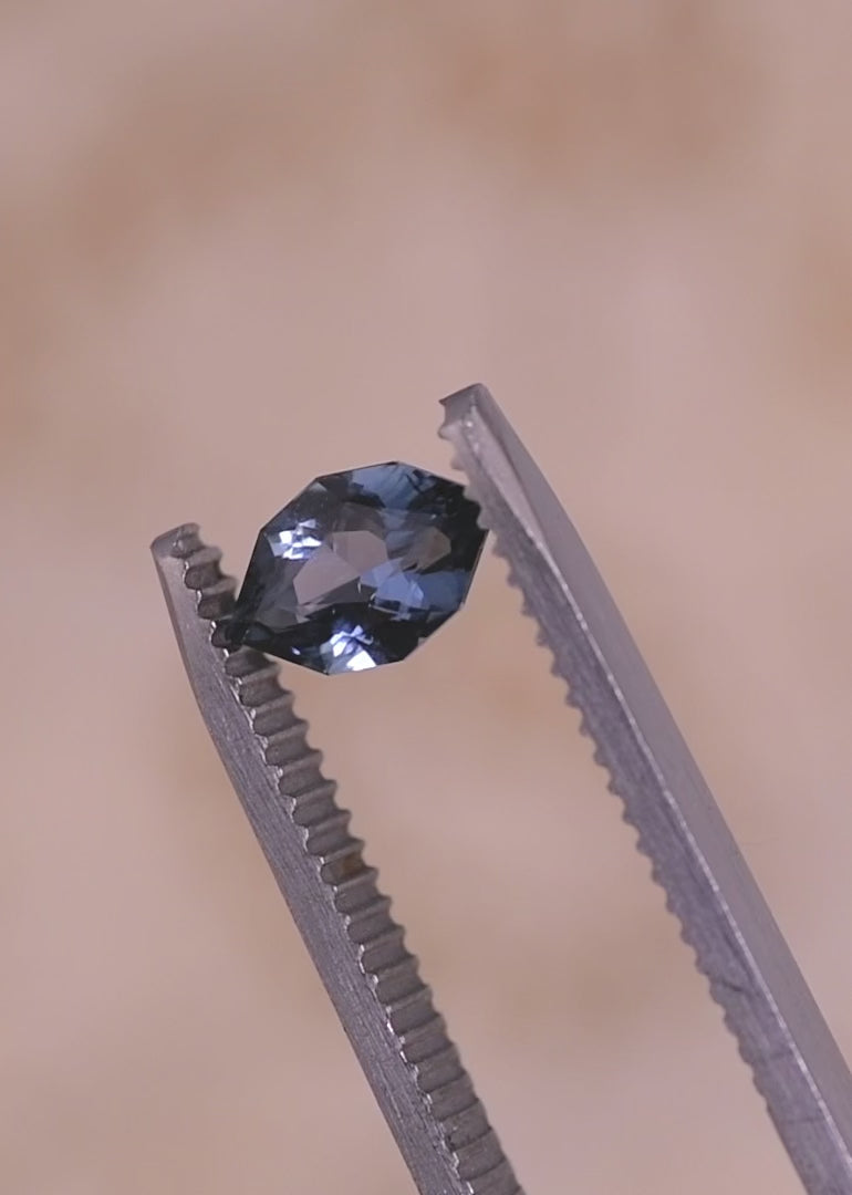 Loose denim blue sapphire turning in tweezers, revealing light reflection and facet pattern in a modified brilliant marquise cut from Madagascar.