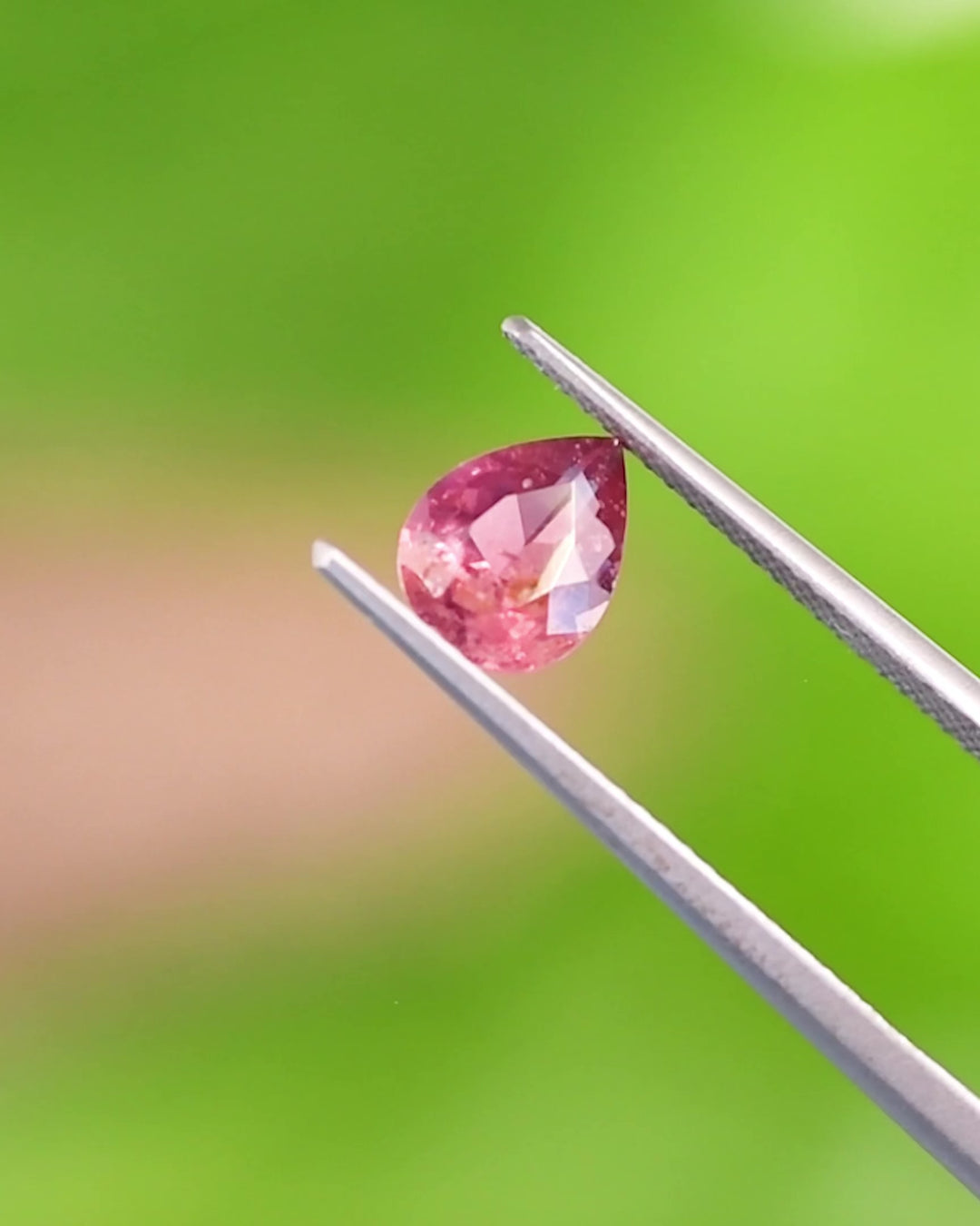 Close-up Video of 1.24CT orange pink red sapphire balanced on fingertip, showing the pear-shaped modified brilliant cut and internal inclusions under natural daylight, unheated gem from Umba River Valley, Tanzania.