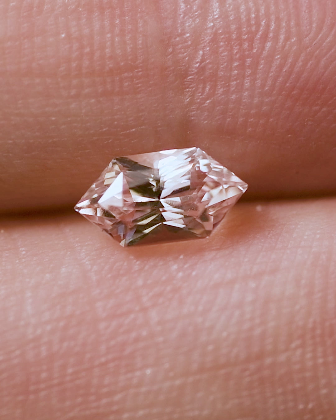 Vertical close-up video of 1.17CT peach pink sapphire reflecting warm hues as it rotates in natural daylight, showing exceptional brilliance and symmetry in the Dutch marquise hexagon cut, natural and unheated from Sakaraha, Madagascar.