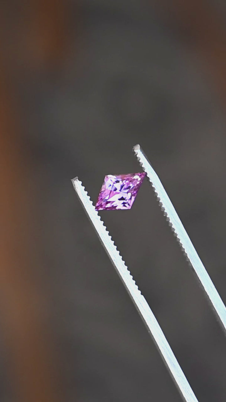 1.15ct hot pink custom kite rhombus cut sapphire rotating in gem tweezers under natural light.