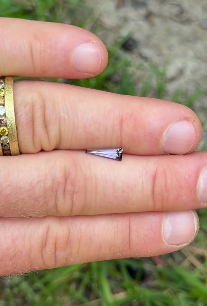 Rotating Tanzanite gemstone under natural light, showing step cut facets with peach, lavender, and gray-violet shifts.