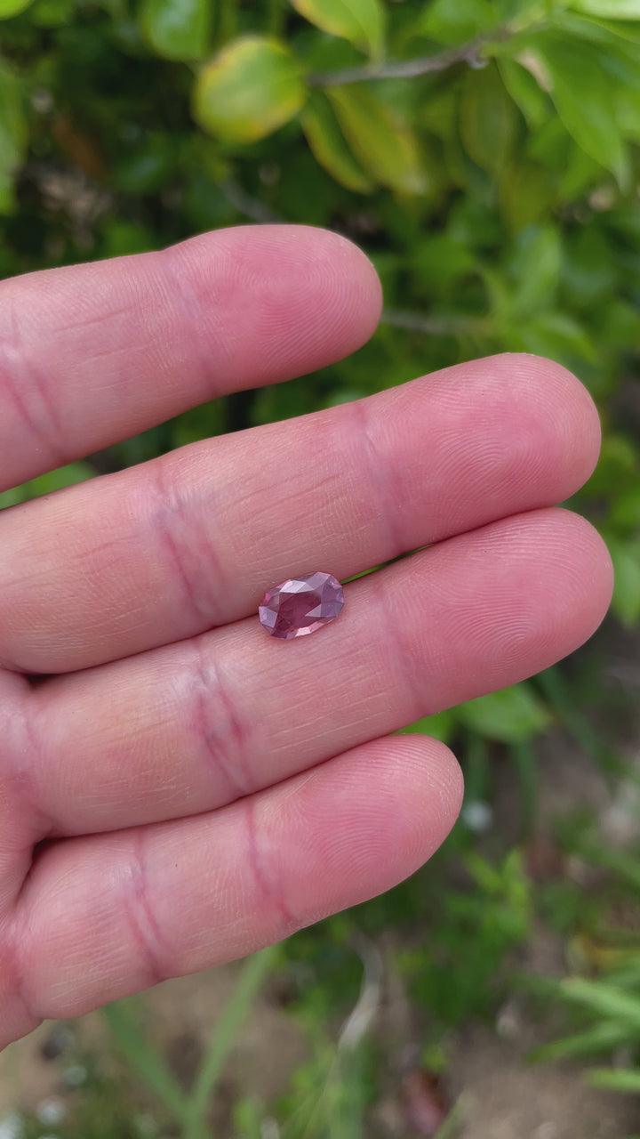 A side perspective of a 1.45-carat pastel grapefruit sapphire, highlighting its cushion cut and gentle pastel hues against a soft, natural backdrop.
