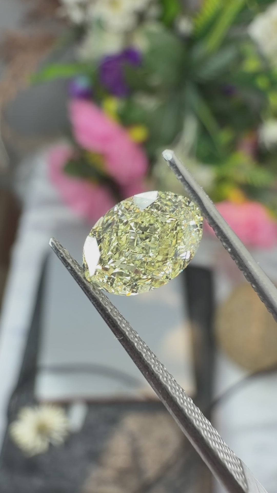 A natural loose yellow oval cut diamond held in gem tweezers under natural light.