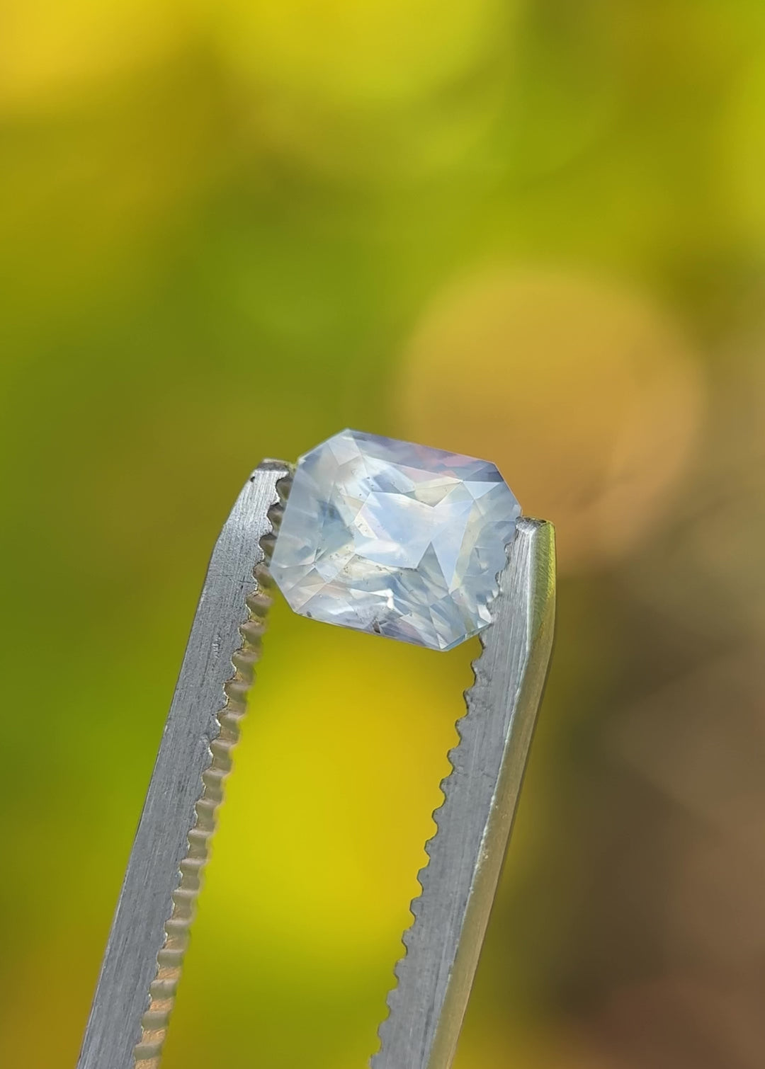 Video of 1.58 carat silver white sapphire from Madagascar rotating in tweezers, revealing radiant cut and opalescent play of light