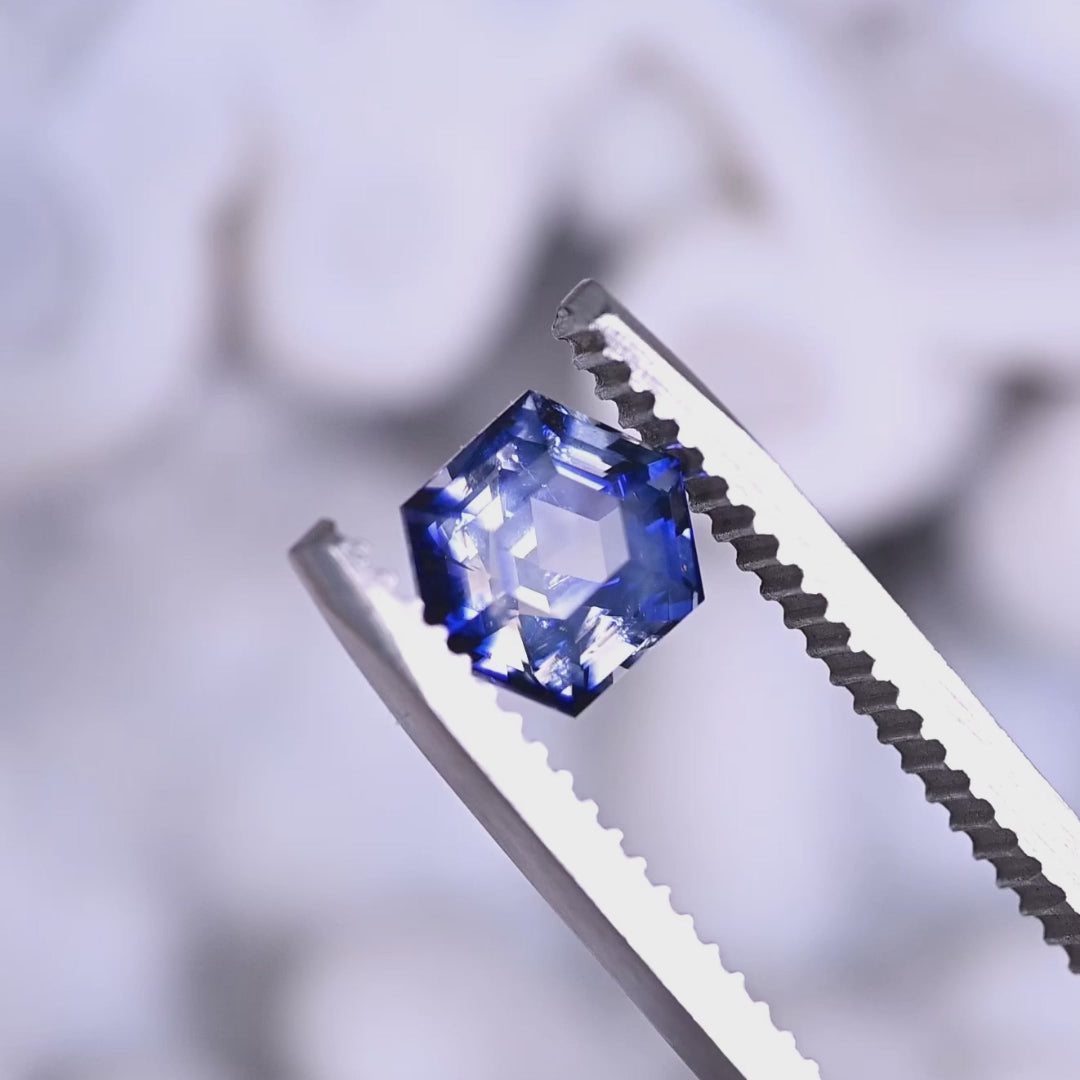 Loose blue and colorless bi‑color sapphire from Ratnapura, Sri Lanka rotating in tweezers, showing the precision hexagon step cut and the contrast between the blue and colorless zones.