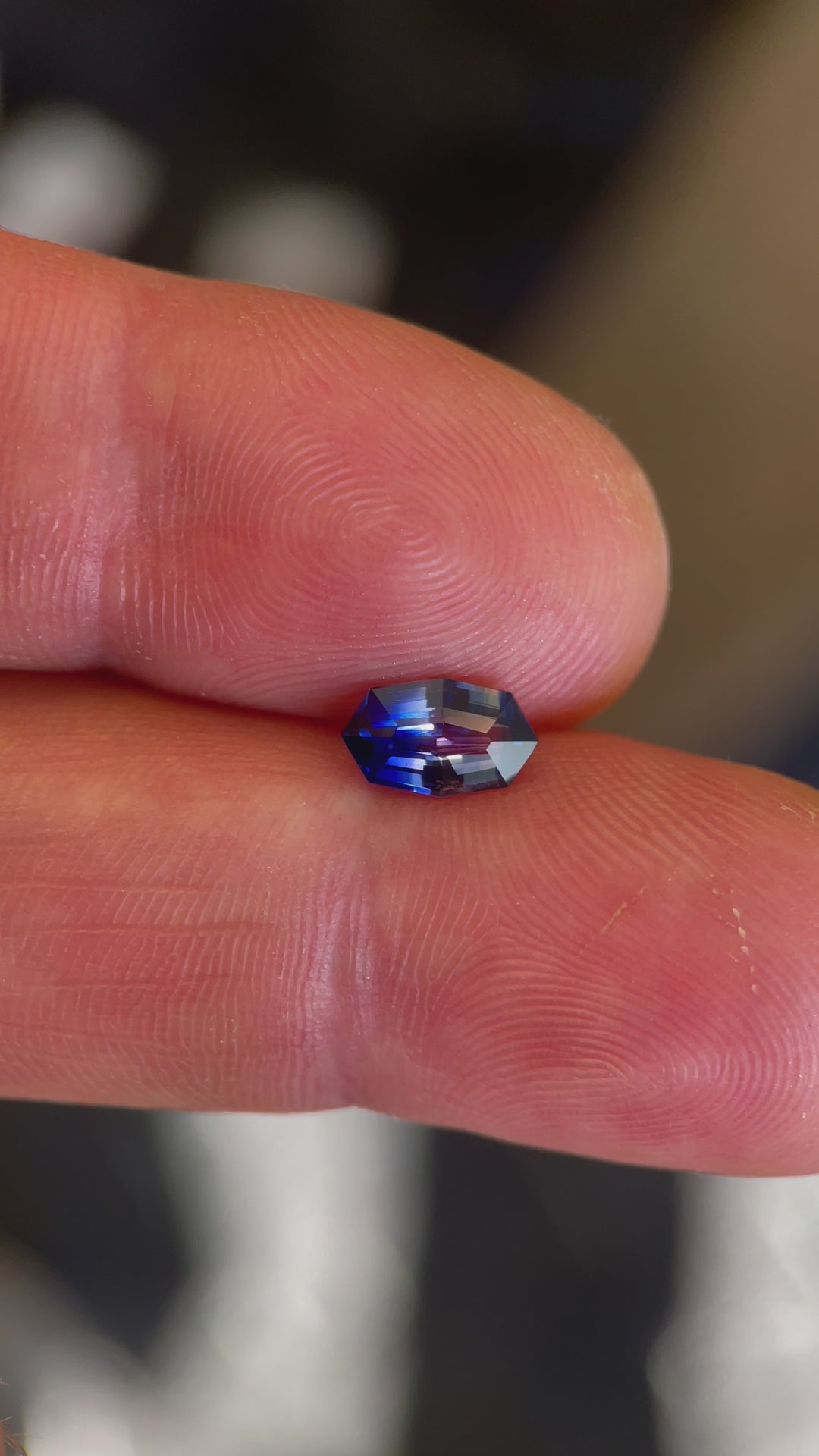 Close-up video of a bi-color 1.03 carat sapphire, held between fingers, emphasizing the stone's precision cut and unique color transition, sourced from Sri Lanka and treated to enhance its appearance.