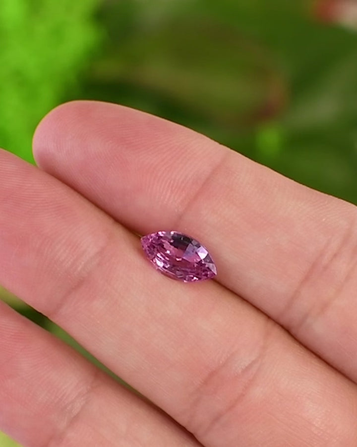 Macro video of 1.65 carat Barbie pink sapphire resting on fingertips, showing flashes of vivid pink light and reflective brilliance of the precision marquise mixed cut, untreated sapphire from Madagascar.