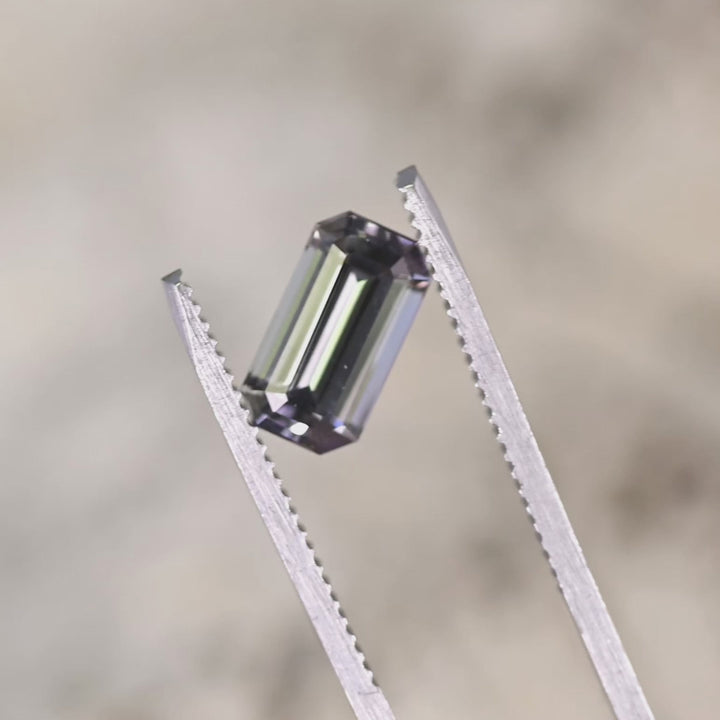 Close-up video of 2.02ct purple green Tanzanite emerald cut held in tweezers, untreated precision faceted gemstone from Tanzania displaying clarity, sparkle and elongated elegant shape