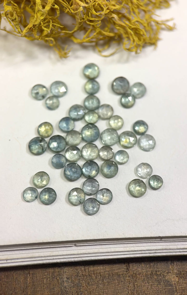 Video showcasing 34 natural teal blue green sapphires from the Eldorado Deposit, Montana, shimmering in natural light to highlight their round rose cut facets and color variations, untreated gemstones totaling 8.05 carats.