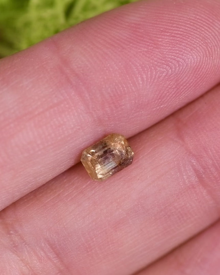 Close-up motion video of 1.11 carat grey, teal, and yellow parti sapphire rotating under natural light, showing reflective step cuts and internal inclusions of its custom emerald cut, unheated gemstone from Umba River Valley, Tanzania.