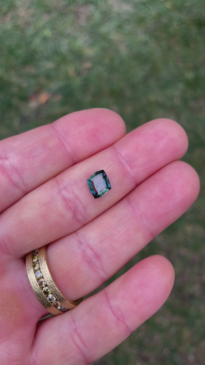 Video of a beautifully cut 1.68-carat no heat sapphire, featuring striking teal and blue colors. The video emphasizes the gem's angles, reflections, and overall quality, captured under natural lighting.