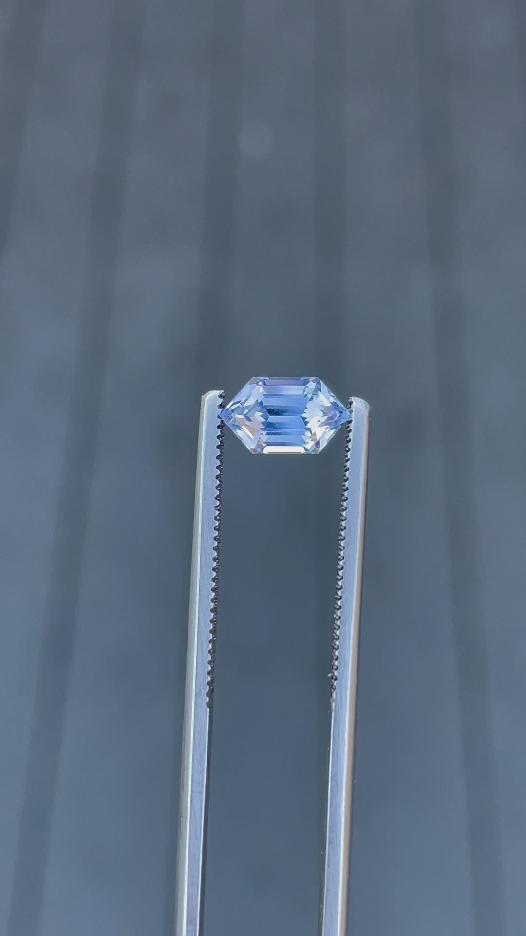 A 1.62-carat light Ceylon blue sapphire rotates slowly in natural light, revealing the precision of its step-cut hexagonal shape. The video captures the play of light across the gem’s facets, showcasing the untreated sapphire’s clear blue color and brilliance. The gem measures 8.78mm by 5.06mm by 4.50mm, sourced from Sri Lanka.