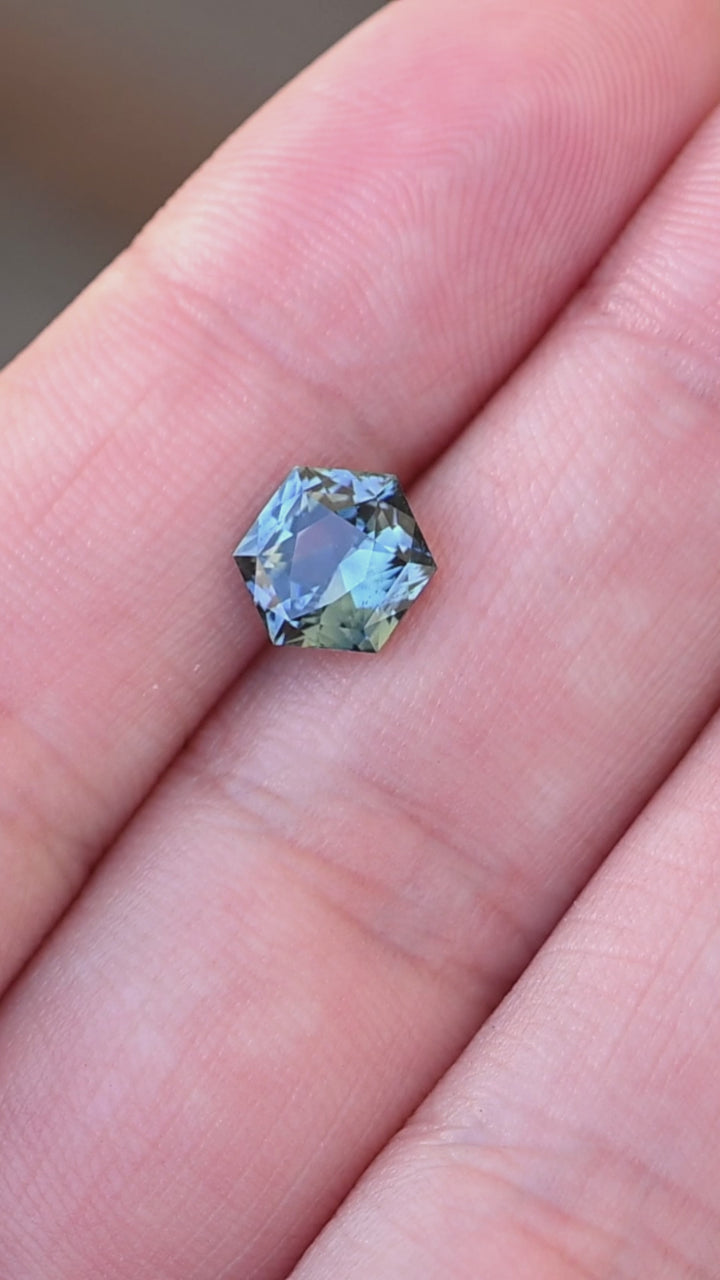 2.03ct blue teal precision hexagonal cut sapphire rotating on fingertips under natural light.