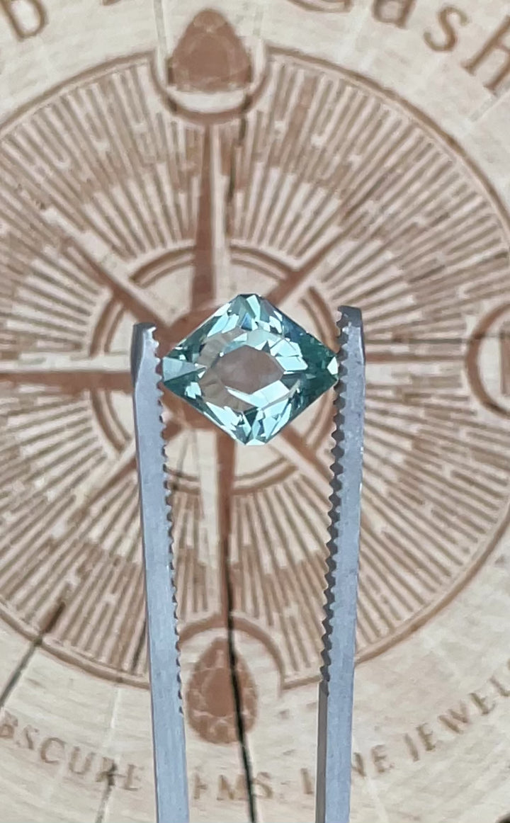 Close-up video of a Montana Sapphire held in tweezers, featuring a custom rhombus antique cut and unheated seafoam teal coloration.