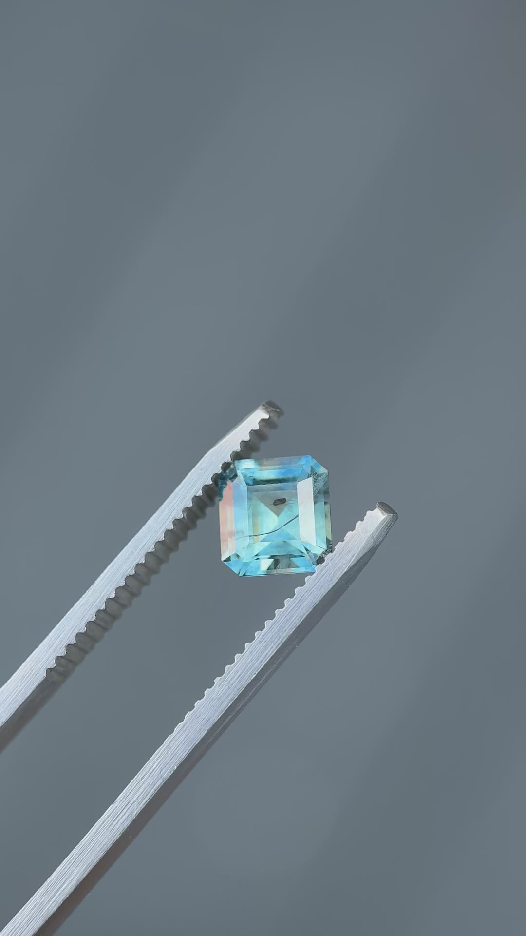 Square step-cut Montana sapphire turned in tweezers under natural light, emphasizing clean lines and depth.