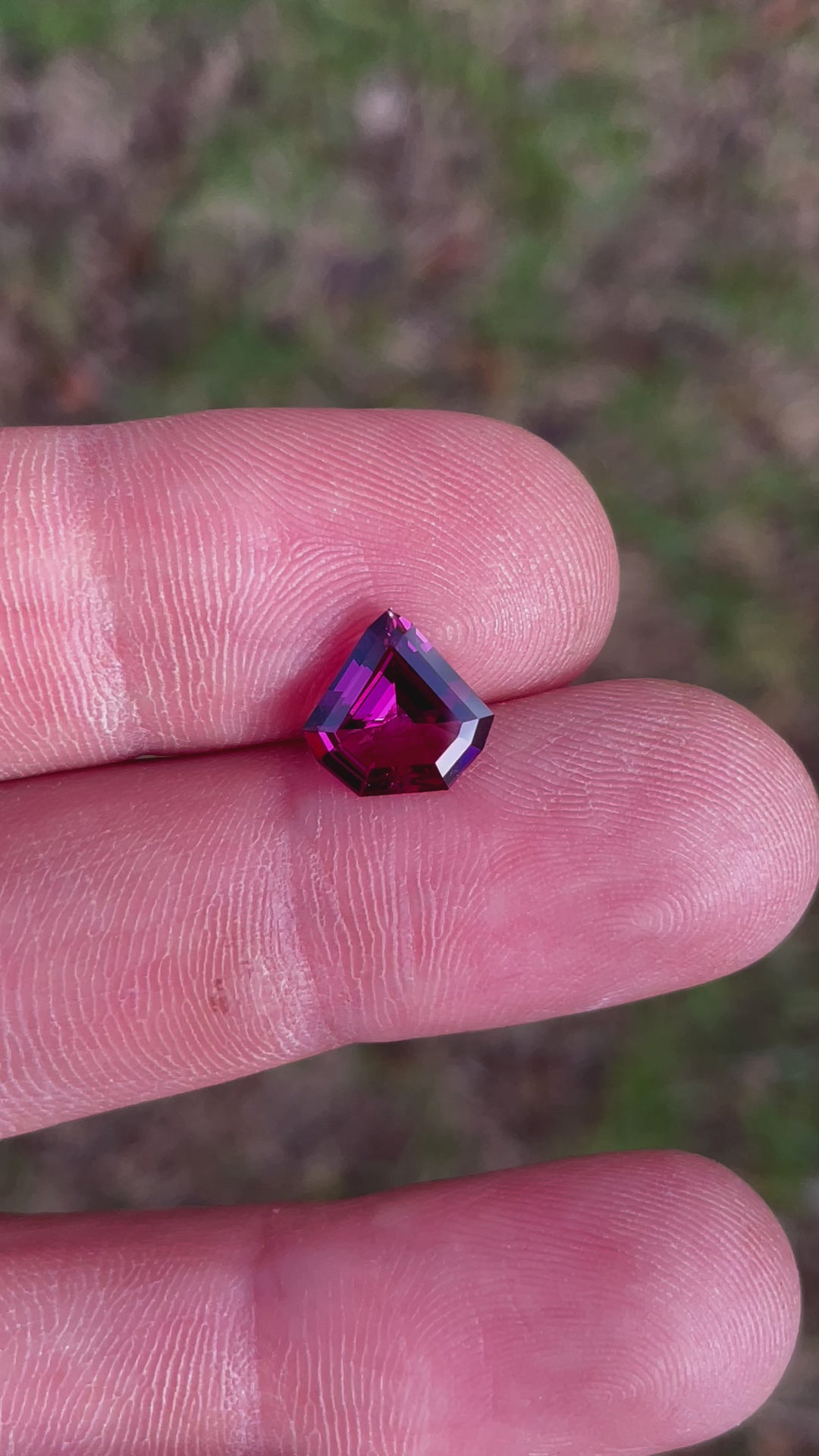 360-degree view of a 2.61 carat shield step cut garnet, featuring brilliant purple, pink, and red colors, untreated and from Tanzania.