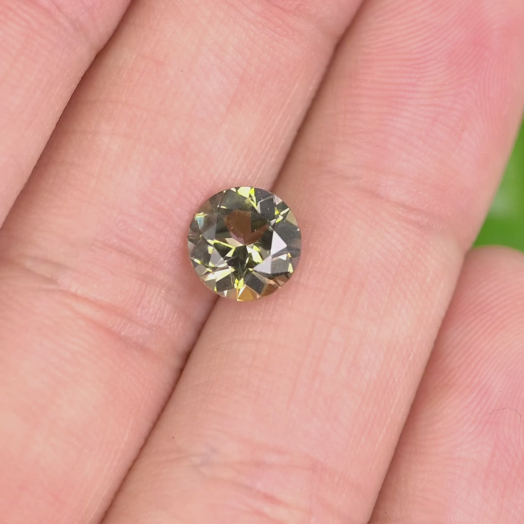 1.65 carat yellow orange green Tanzanite round cut rotating under natural light, custom mix faceted gemstone from Merelani Hills Tanzania showing vivid color shift and sparkle for custom jewelry