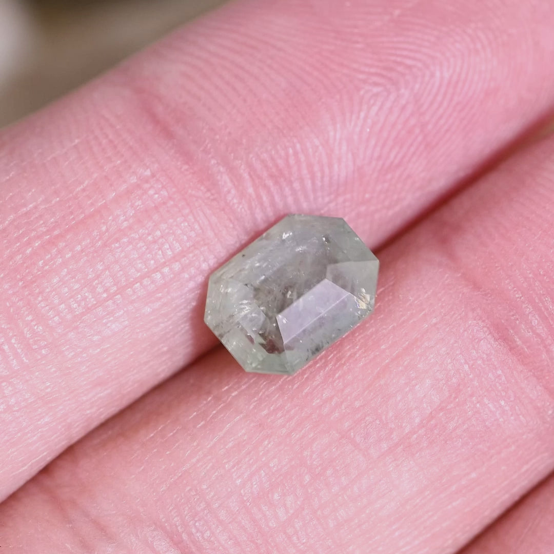 Seafoam green Montana sapphire rotated by hand, revealing depth of the thick portrait cut, shifting mint-to-celadon tones, and internal inclusions catching light as the stone tilts.