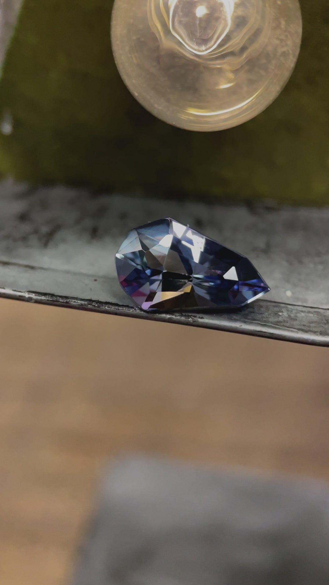 A beautiful tanzanite gemstone weighing 3.31 carats, shimmering in shades of gray, blue, and purple with a modified pear cut, recorded in dynamic motion to highlight its brilliance.