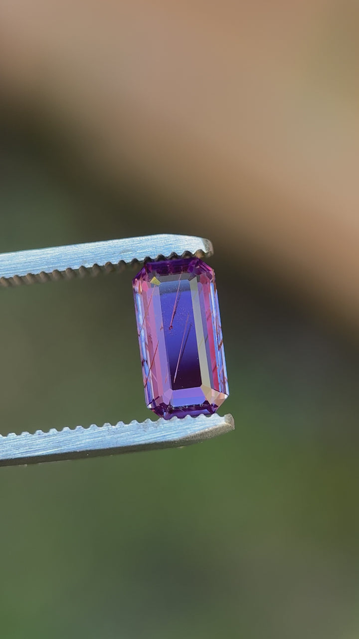 Close-up video of rutilated purple sapphire held in tweezers under natural light, demonstrating precision emerald portrait cut facets, internal rutile inclusions, brilliance, and untreated sapphire clarity from Sakaraha, Madagascar