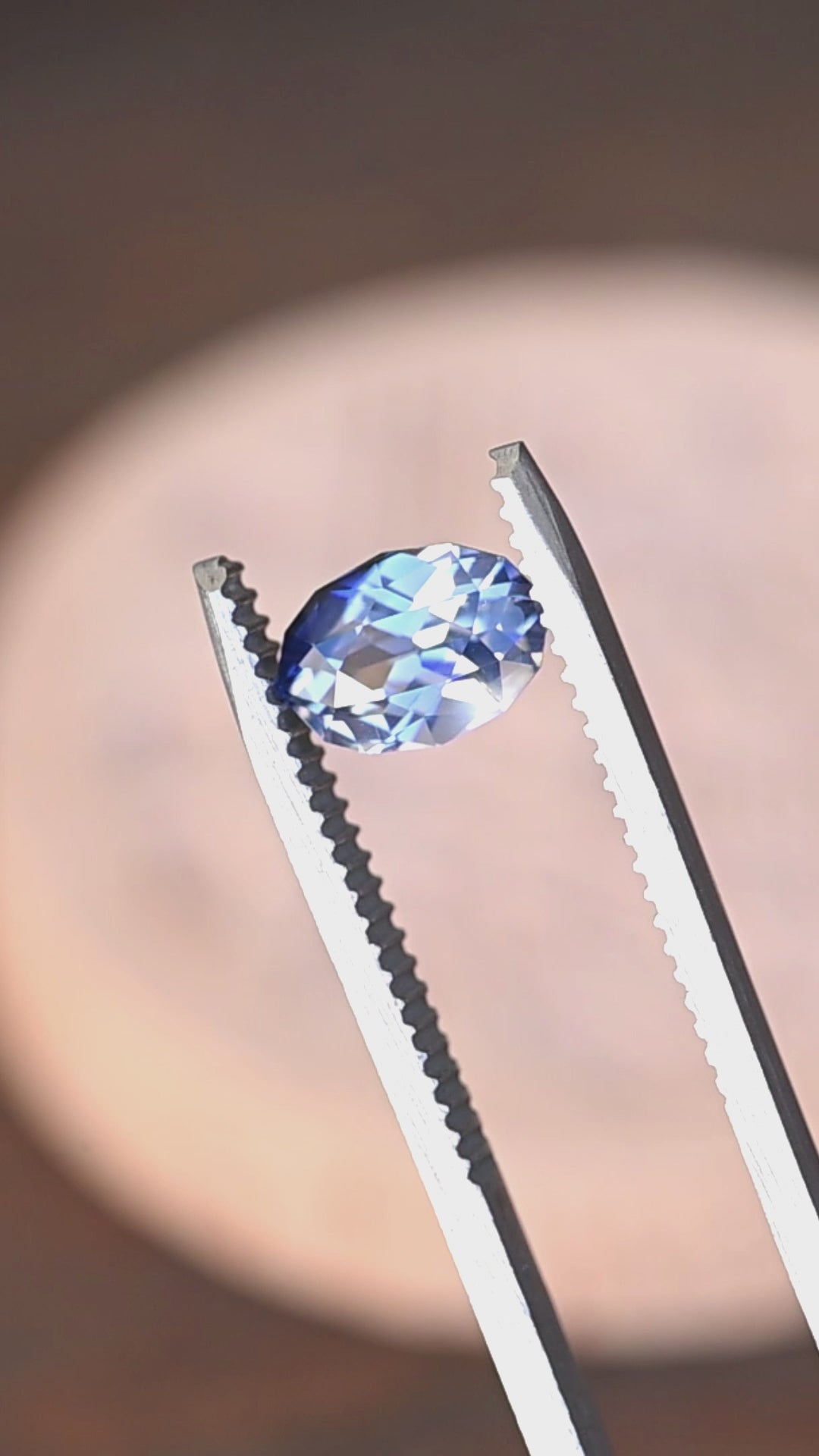 1.85ct blue and white parti sapphire in a custom moval brilliant cut from Sri Lanka rotating in gem tweezers under natural light.