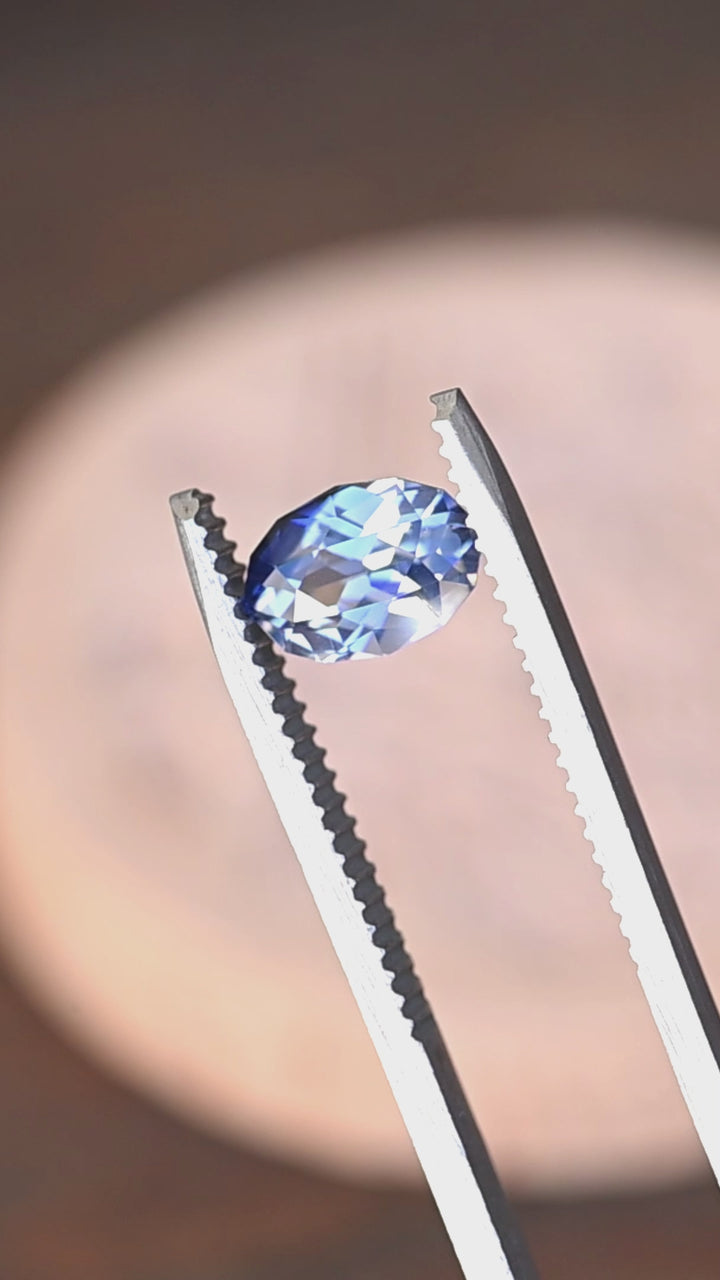 1.85ct blue and white parti sapphire in a custom moval brilliant cut from Sri Lanka rotating in gem tweezers under natural light.