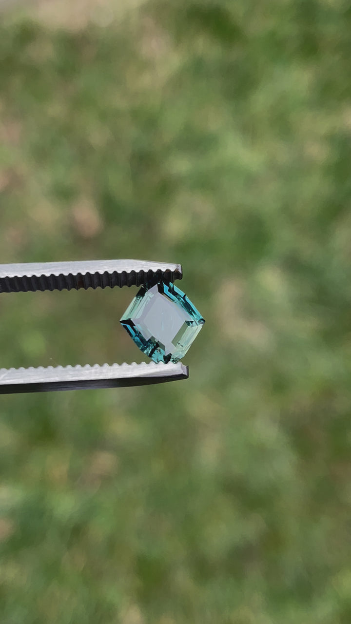 Video showcasing a 1.68-carat teal-blue no heat sapphire with a custom geometric rhombus portrait cut, highlighting the gemstone's brilliance and natural luster as it is rotated under different lighting conditions.