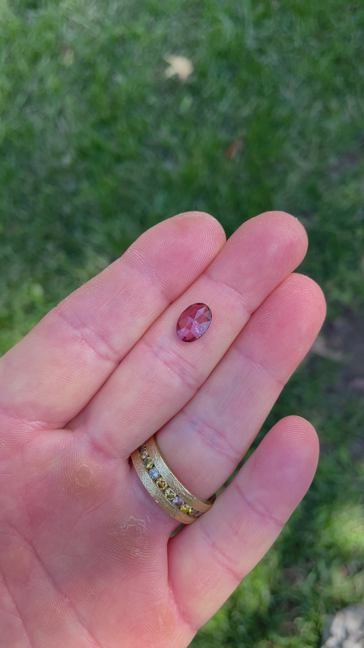 Video of a 1.57-carat oval cut sapphire showcasing vibrant ruby-red and orange hues under natural lighting.