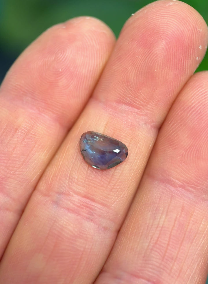 Unheated blue and yellow parti sapphire rotated in hand, showing shifting contrast between inky blue edges and golden-yellow flashes across the rose-cut crown.