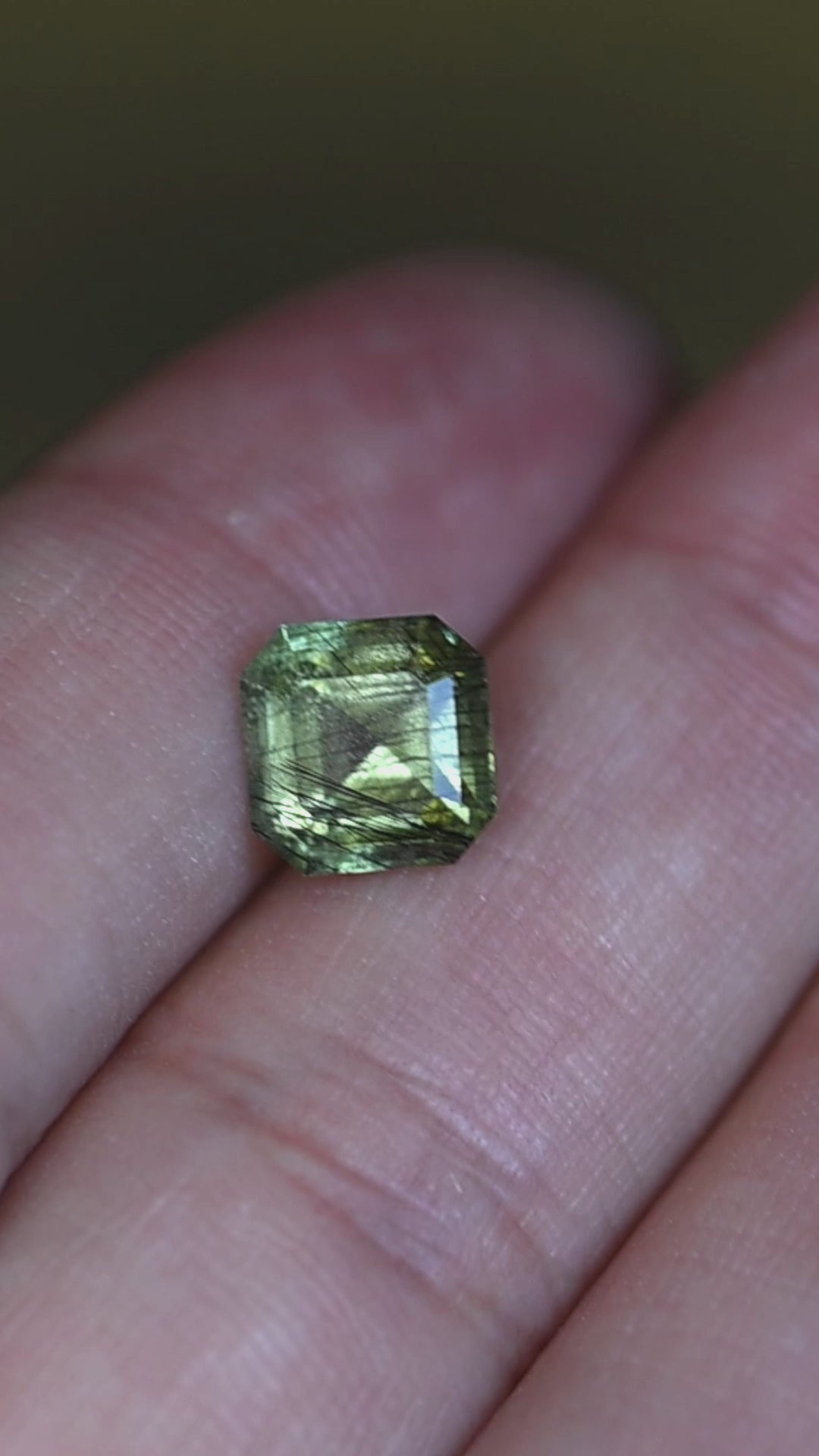Experience the refined beauty of this untreated Pakistan peridot in hand, displaying its tranquil sage green color, custom Asscher cut, and naturally occurring crystalline inclusions.