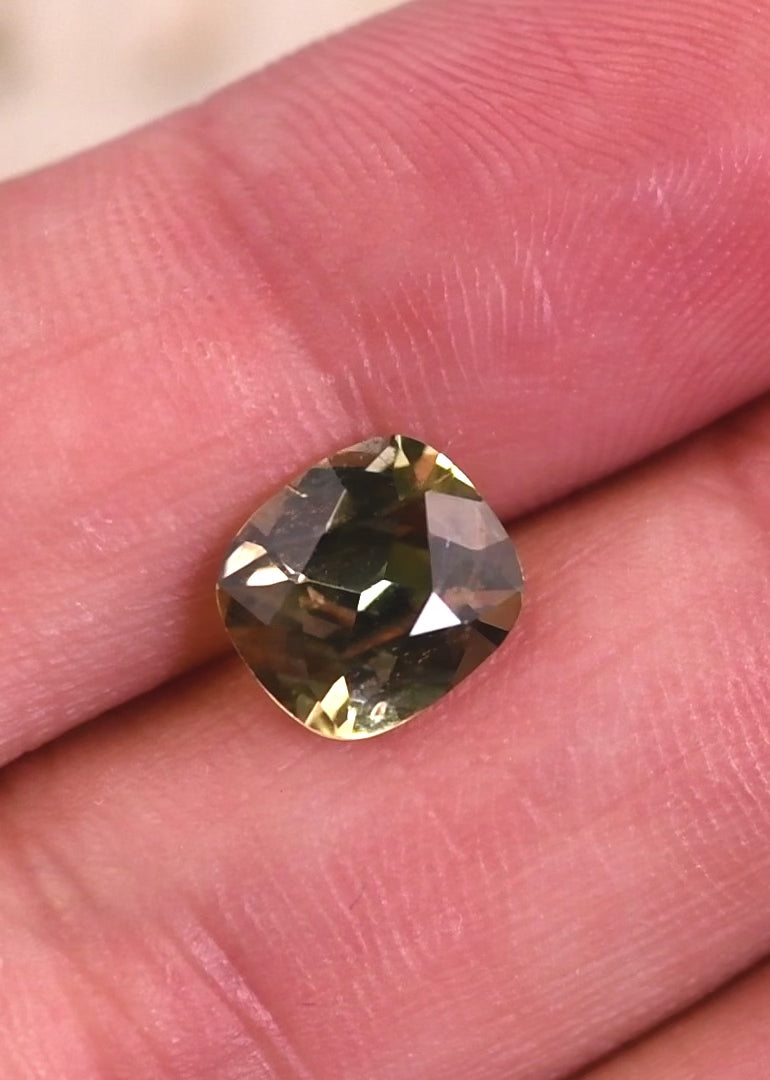 Video of natural yellow green Tanzanite cushion brilliant cut rotating under light, demonstrating sparkle, facet reflections, and untreated color from Merelani Hills, Tanzania